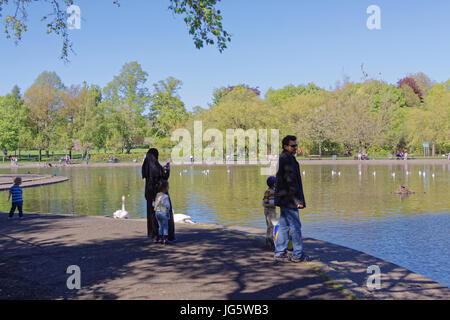 Asiatische Familie Flüchtling Mutter Vater gekleidet Hijab Schal Weiher in UK alltägliche Szene Mutter und Kind in Queens Park Glasgow Stockfoto