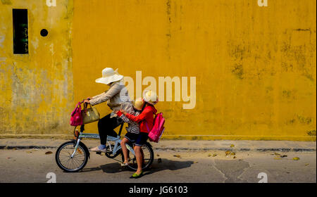 Eine Frau fährt ein Fahrrad mit zwei kleinen Kindern auf dem Rücken in die Altstadt von Hoi an, Vietnam Stockfoto