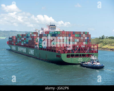 Ein Containerschiff Xin Mei Zhou der China Reederei auf der Durchreise Gatun See des Panama-Kanals, gesteuert von einem Schlepper Stockfoto