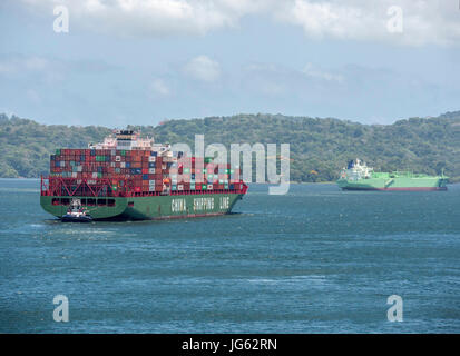 Ein Containerschiff Xin Mei Zhou der China Reederei auf der Durchreise Gatun See des Panama-Kanals, gesteuert von einem Schlepper Stockfoto