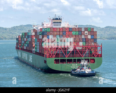 Ein Containerschiff Xin Mei Zhou der China Reederei auf der Durchreise Gatun See des Panama-Kanals, gesteuert von einem Schlepper Stockfoto