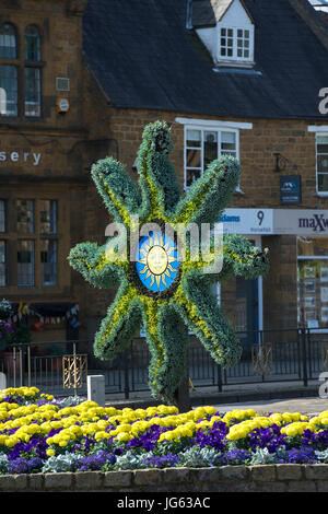 Floral Sonne Symbol Skulptur und bunten Blumenbeet vor Banbury cross, im Licht frühen Morgens. Oxfordshire, England Stockfoto