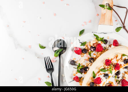 Sommer Früchte Beeren Frühstück. Gesunde Bananensplit Frühstück mit Frischkäse, Himbeeren, Brombeeren, Minze, weiß und rosa Schokolade. Auf weiß ma Stockfoto