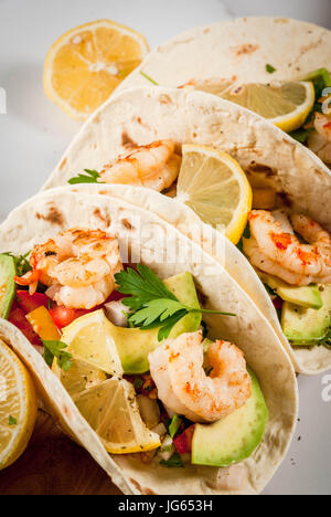 Fisch und Meeresfrüchte. Mexikanisches Essen. Tortilla-Tacos mit traditionellen hausgemachten Salsa Salat, Petersilie, frische Zitrone, Avocado und gegrillte Garnelen Bauern. Auf weißem Marmor Stockfoto