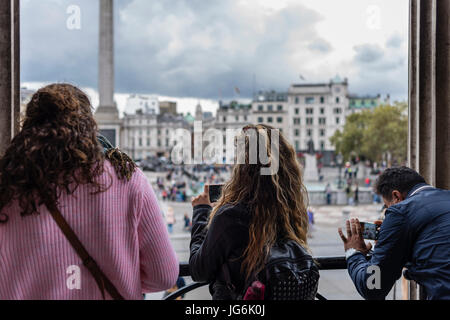 Touristen auf der Suche nach unten zum Trafalgar Square und die Fotos vom Balkon der National Gallery, London, UK Stockfoto