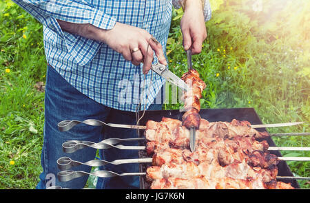 Leckere, saftige Grill, am Spieß über offenem Feuer gebraten, an einem sonnigen Tag. Hand geschnitten Fleisch mit einem Messer. Die horizontalen Rahmen. Stockfoto