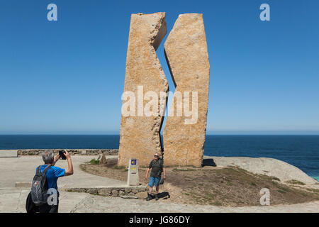 Menschen fotografieren vor der Skulptur Hommage "Pedra da Ferida" ("Wunde Stein") von spanischen Bildhauers Alberto Bañuelos gewidmet die Freiwilligen, die geholfen haben, reinigen Sie die Prestige-Ölpest im Jahr 2002 an der Küste des Atlantischen Ozeans, bekannt als der Costa De La Muerte (Todesküste), in der Nähe der Stadt Muxía in Galicien, Spanien. Der Meilenstein des Camino de Santiago (Jakobsweg) im Vordergrund zu sehen. Stockfoto