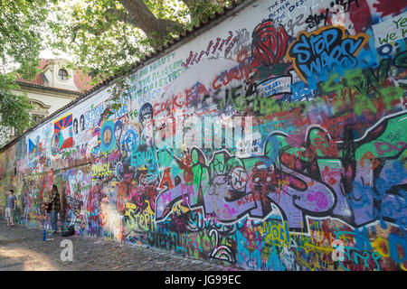 Ein Tourist und Straßenmusiker an der John-Lennon-Mauer in Prag. Es ist eine Wand mit Stücken von songtexte von Beatles Songs und John Lennon inspirierten Graffiti. Stockfoto