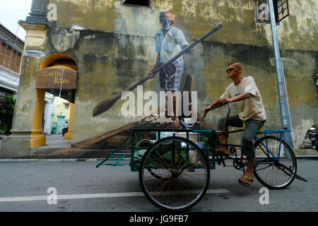 Ein chinesischer Mann reitet auf seinem Fahrrad vorbei an einem riesigen Wandbild in Georgetown, Penang, Malaysia Stockfoto