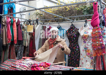 LONDON, ENGLAND - 12. Juli 2017 der Verkäufer des Schals auf der Portobello Road vor dem Hintergrund der bunten indischen Schals Stockfoto