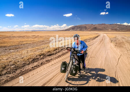 Frau Radrennfahrer kämpfen und schieben ihr Fahrrad auf Wellpappe Sandweg im Altiplano in Bolivien Stockfoto