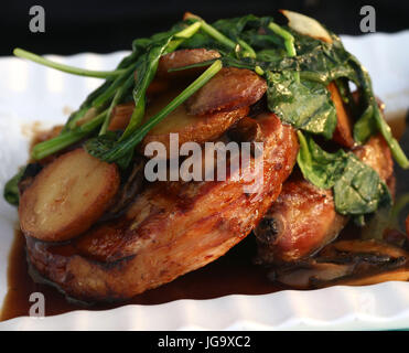 Verwelkt Spinat über Schweinekoteletts mit Pilz-Soße und Bratkartoffeln auf weiße gerippte Schale Stockfoto