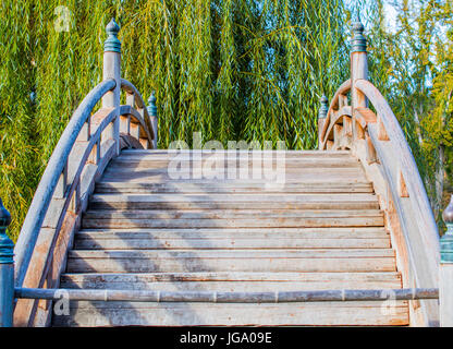 Blick geradeaus auf verwitterten hölzernen Bogenbrücke im japanischen Garten Stockfoto