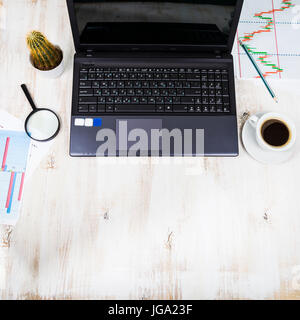 Arbeitsplatz der Geschäftsmann mit einem Laptop und Geschäftspapiere. Auf dem Tisch sind Kaffee, Laptop, Lupe, Grafiken und Cactus Stockfoto