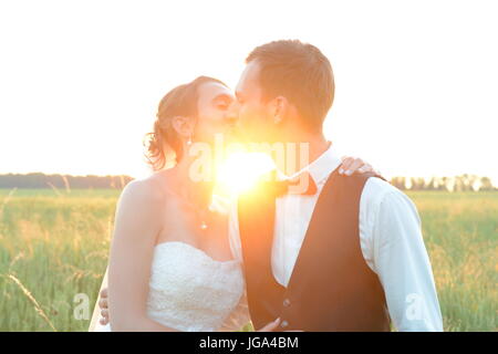 frisch verheiratetes Paar ist gegenseitig beim Sonnenuntergang im Freien in einem Feld zu küssen Stockfoto