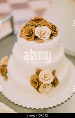 Nahaufnahme der weiße Hochzeitstorte mit Chocolade Rosen verziert. Stockfoto