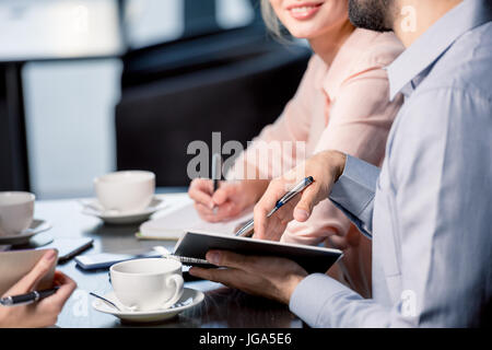 Close-up Teilansicht des Jugendlichen Kaffee trinken und in Notizbüchern bei Geschäftstreffen, Mittagessen Geschäftskonzept schreiben Stockfoto