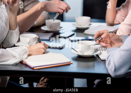 Close-up Teilansicht des Jugendlichen Kaffee trinken und in Notizbüchern bei Geschäftstreffen, Mittagessen Geschäftskonzept schreiben Stockfoto
