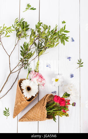 Draufsicht der schönen Blüte Blumen und grünen Blättern in leckere Waffel Kegel Stockfoto