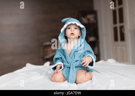 Glückliches Baby junge im blauen Gewand posiert auf Bett Stockfoto