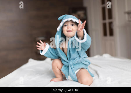 Glückliches Baby junge im blauen Gewand posiert auf Bett Stockfoto