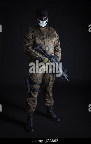 Anti-Terrorist in schwarzer Maske hält eine Pistole auf schwarzem Hintergrund Stockfoto