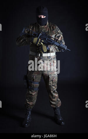 Anti-Terrorist in schwarzer Maske hält eine Pistole auf schwarzem Hintergrund Stockfoto