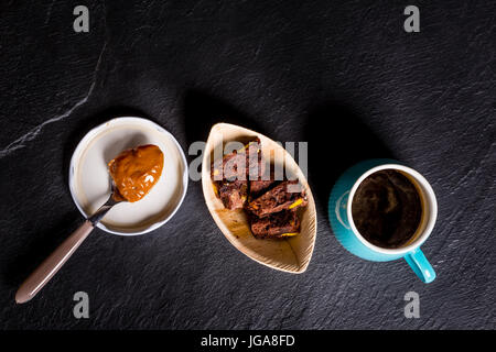 Dulce de Leche in einem Löffel, sehr süßen Crème Caramel oder Praline Creme aus Argentinien, schwarzen Kaffee Cand einige Schokoladenkekse. Stockfoto