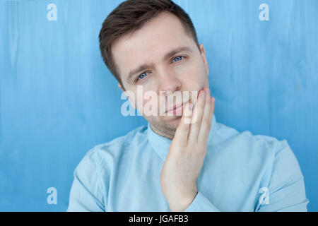 Kaukasische nachdenklicher junger Mann stehend durch die blaue Woodenwall. Stockfoto