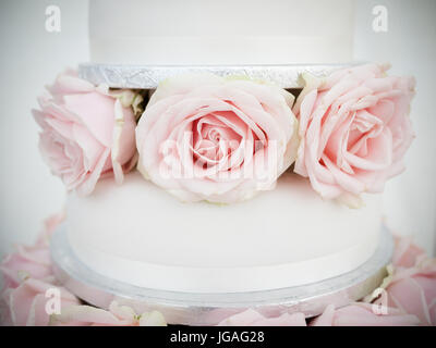 Eine Nahaufnahme von einer Hochzeitstorte mit rosa Rosen und weißen Zuckerguss in Pastellfarben Stockfoto