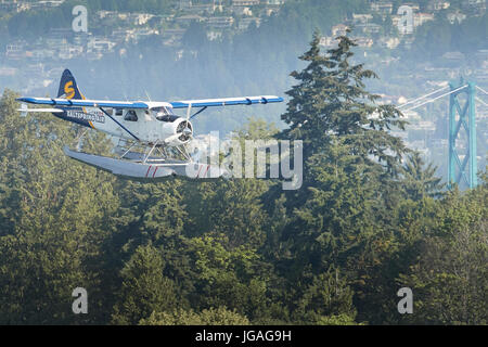 Ein vintage Harbour Air Wasserflugzeuge de Havilland DHC-2 Beaver fliegen über die Lions Gate Bridge in Vancouver, British Columbia, Kanada. Stockfoto