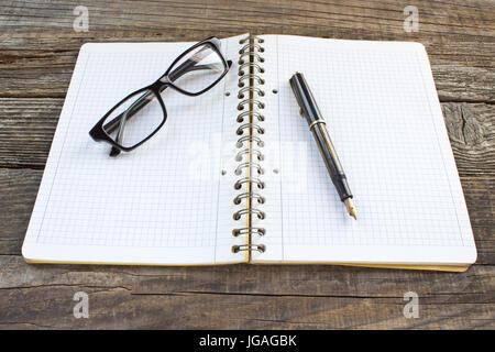 Füllfederhalter und Spiral-Notizbuch mit Brille auf Holztisch Stockfoto