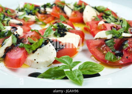 Caprese-Salat. Tomatenscheiben, Mozzarella und zerkleinerten Basilikum, gegossen mit Öl und Essig, bestreut mit Salz und Pfeffer Verlegung auf weißen Plat Stockfoto