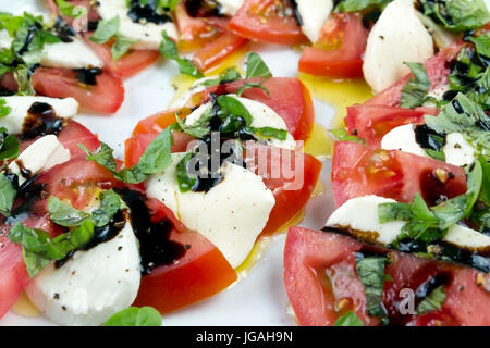 Caprese-Salat. Tomatenscheiben, Mozzarella und zerkleinerten Basilikum, gegossen mit Öl und Essig, bestreut mit Salz und Pfeffer Verlegung auf weißen Plat Stockfoto