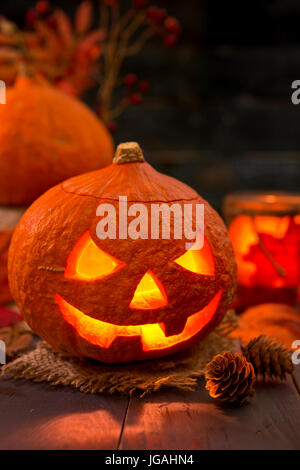 Brennen von Jack O'Lantern auf einem rustikalen Tisch mit herbstlichen Dekorationen, beleuchtet dunkel. Stockfoto