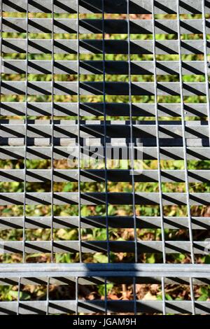 Metallgitter mit Löchern über einer Wiese in Schatten- und Sonnenoptik Stockfoto