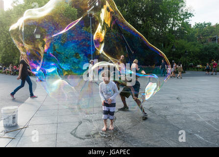 New York, NY, USA - 20. Juli 2015 - A Boy lachend, als er riesige Seifenblasen mit Hilfe des Verkaeufers Blase in Washington Square Park © Stacy Walsh Rosenstock macht Stockfoto