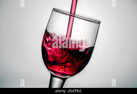 Gießen Rotwein auf einer geneigten in klarem Kristall Glas Kelch mit Bläschen. über weiße Hintergrundbeleuchtung Hintergrund Stockfoto