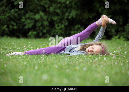 Ein sechs Jahre altes Mädchen üben Yoga auf einer Wiese im Park Stockfoto