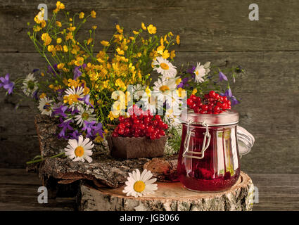 Der Saft aus den Beeren des Viburnum in Glasbehältern auf einer Serviette neben einem Bouquet von wilden Blumen auf einem Holzständer. Rustikale. Stockfoto