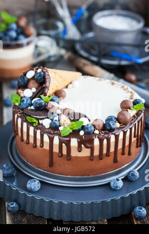 Drei Schoko-Mousse-Kuchen mit Waffelhörnchen, frische Heidelbeeren, Minze, Bonbons und Zuckerguss verziert Stockfoto