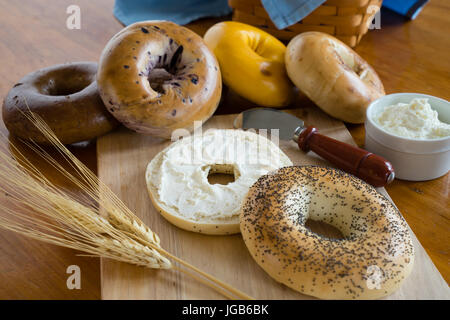 Mohn-Bagel mit Frischkäse mit einem Korb von sortierten Bagels im Hintergrund. Stockfoto