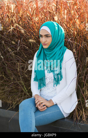 Ernste junge muslimische Frau tragen Hijab sitzen im freien Stockfoto