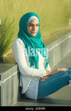 Ernste junge muslimische Frau tragen Hijab sitzen im freien wegschauen Stockfoto