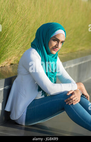 Ernste junge muslimische Frau tragen Hijab sitzen im freien wegschauen Stockfoto