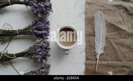 Nahaufnahme von der Tasse Kaffee, umgeben von kleinen Sträußen von trockenen Lavendel und Feder. Vintage Zusammensetzung. Stockfoto