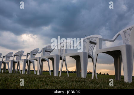 Weiße Plastikstühle auf einer Wiese in einem Kreis für Meditation angeordnet. Stockfoto