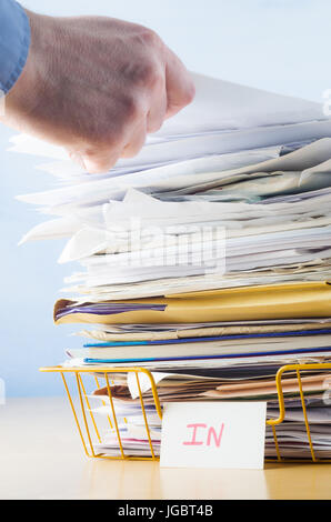 Firmen-Image einer männlichen Hand mit blauem Hemd Manschette sichtbar, hinzufügen oder Entfernen von Dokument von hohen Stapel im Büro im Fach überfüllt. Stockfoto