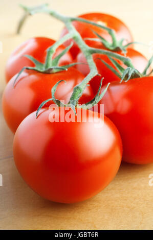 Nahaufnahme von sechs Reife rote Salat Tomaten mit vier noch an Reben und ruht auf Laminat Holztisch.  Schoss knapp über Augenhöhe mit wichtigsten focu Stockfoto