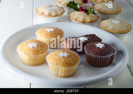 Eine Auswahl an individuellen vergoldet Weihnachten Kuchen und Mince Pies in Folie Gerichte auf einem alten Bauernhaus Küchentisch, bestreut mit Puderzucker in der sh Stockfoto